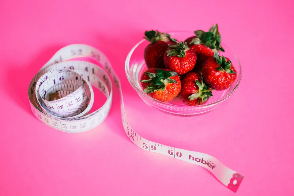 A coiled tape measure marked in centimetres next to a glass bowl of strawberries